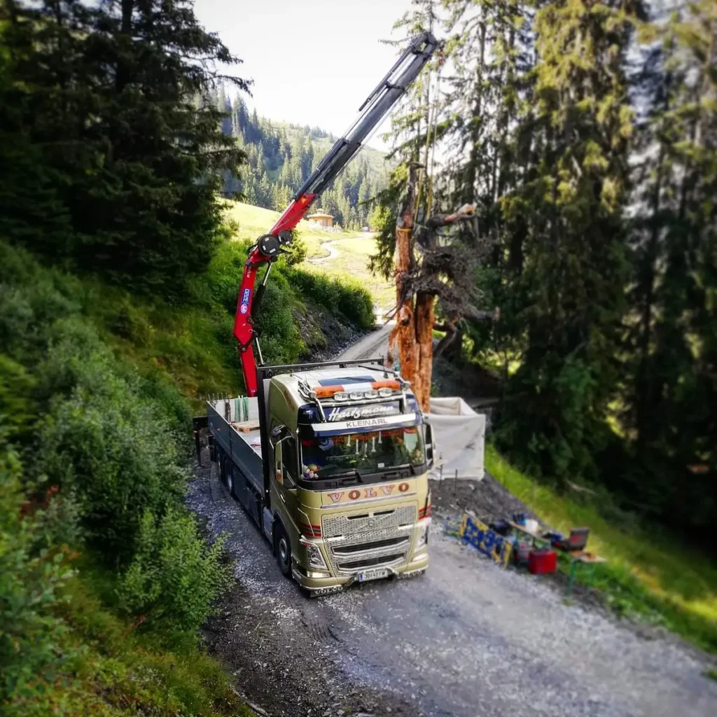 Haitzmann Volvo LKW mit Kran hebt Baumstamm auf Waldweg bei Baustofftransport in Kleinarl