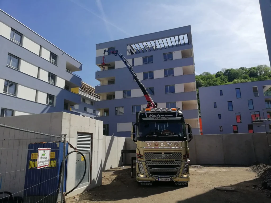 Goldener Volvo LKW mit Kran auf einer Baustelle vor modernen Wohngebäuden bei klarem Himmel in Kleinarl