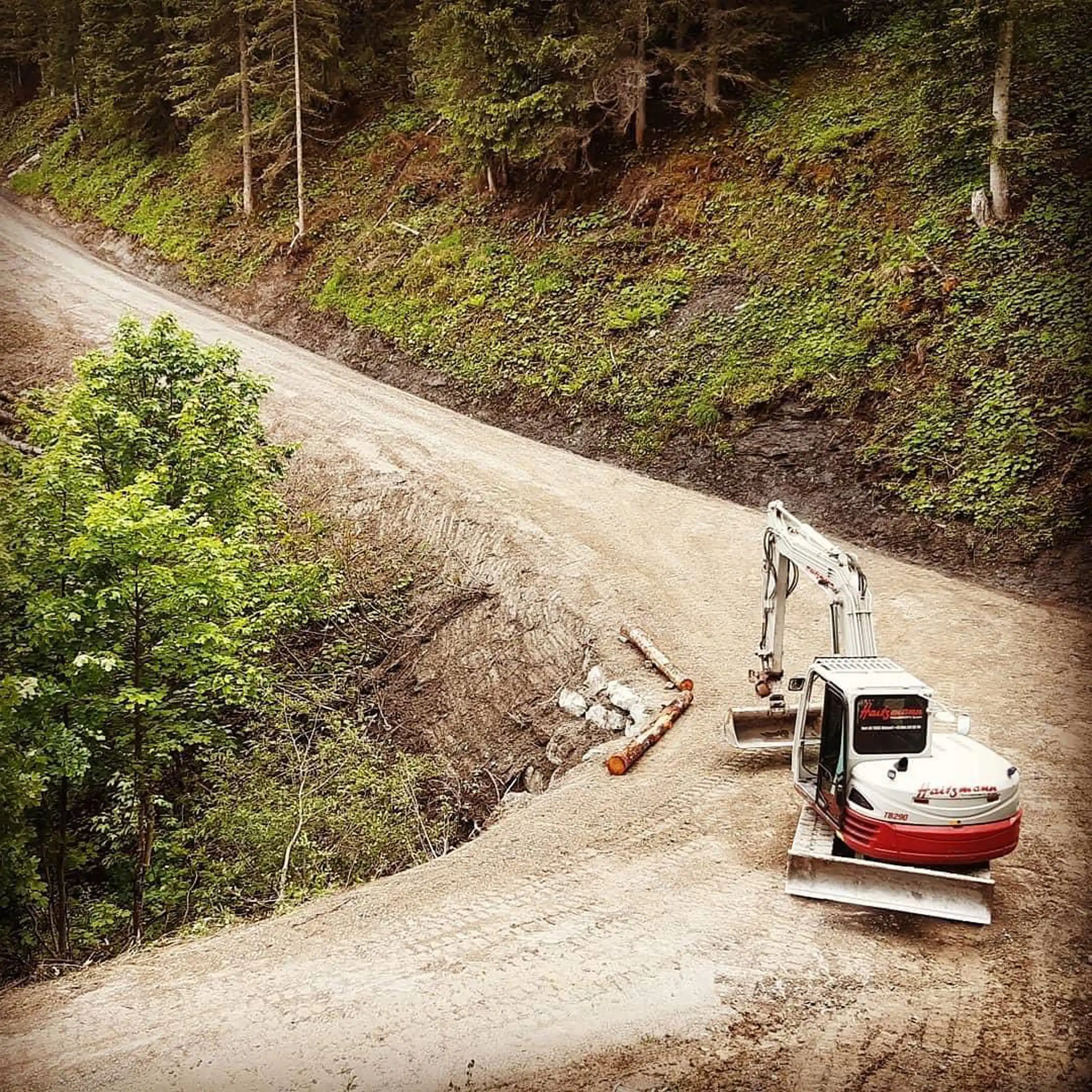 Bagger der Firma Haitzmann Transporte arbeitet auf einem Waldweg in Kleinarl umgeben von Bäumen und Erdarbeiten